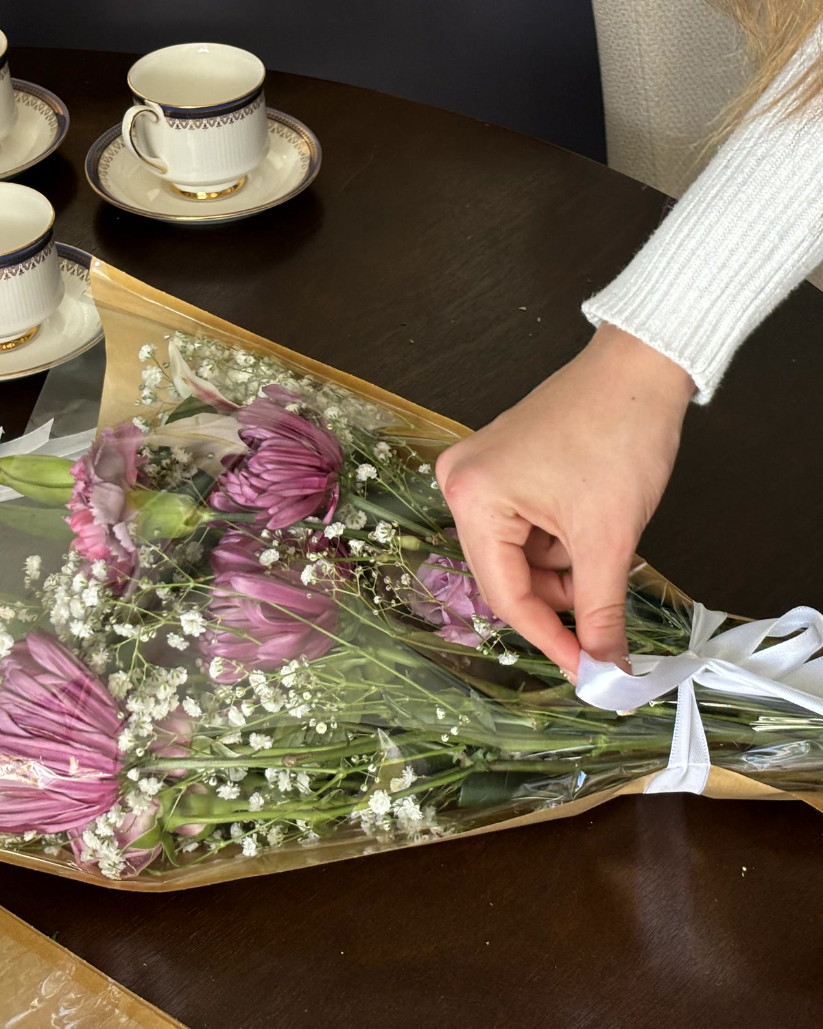 Hands tying a white ribbon around a paper-wrapped bouquet