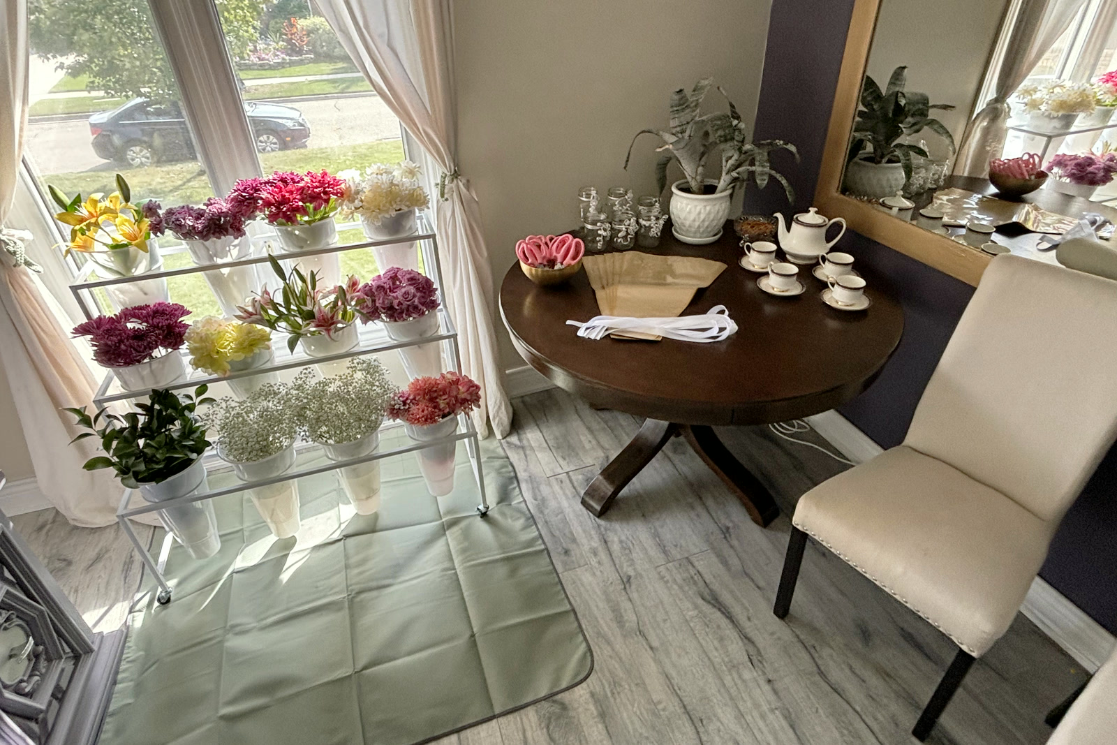 The bouquet bar set up by a window: a tiered stand of flowers in white buckets, and a round table with snips, paper and teacups